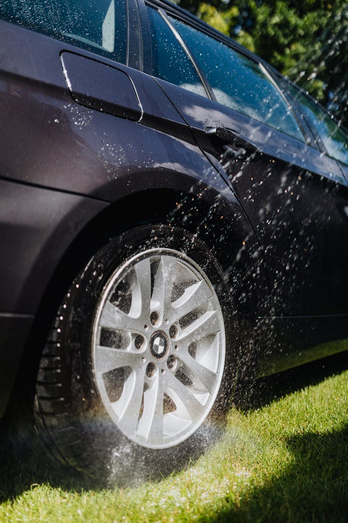 A car tire being washed with water outdoors on a sunny day. Perfect for cleanliness themes.